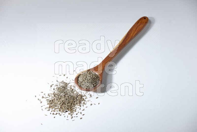 A wooden ladle full of cumin seeds on a white flooring