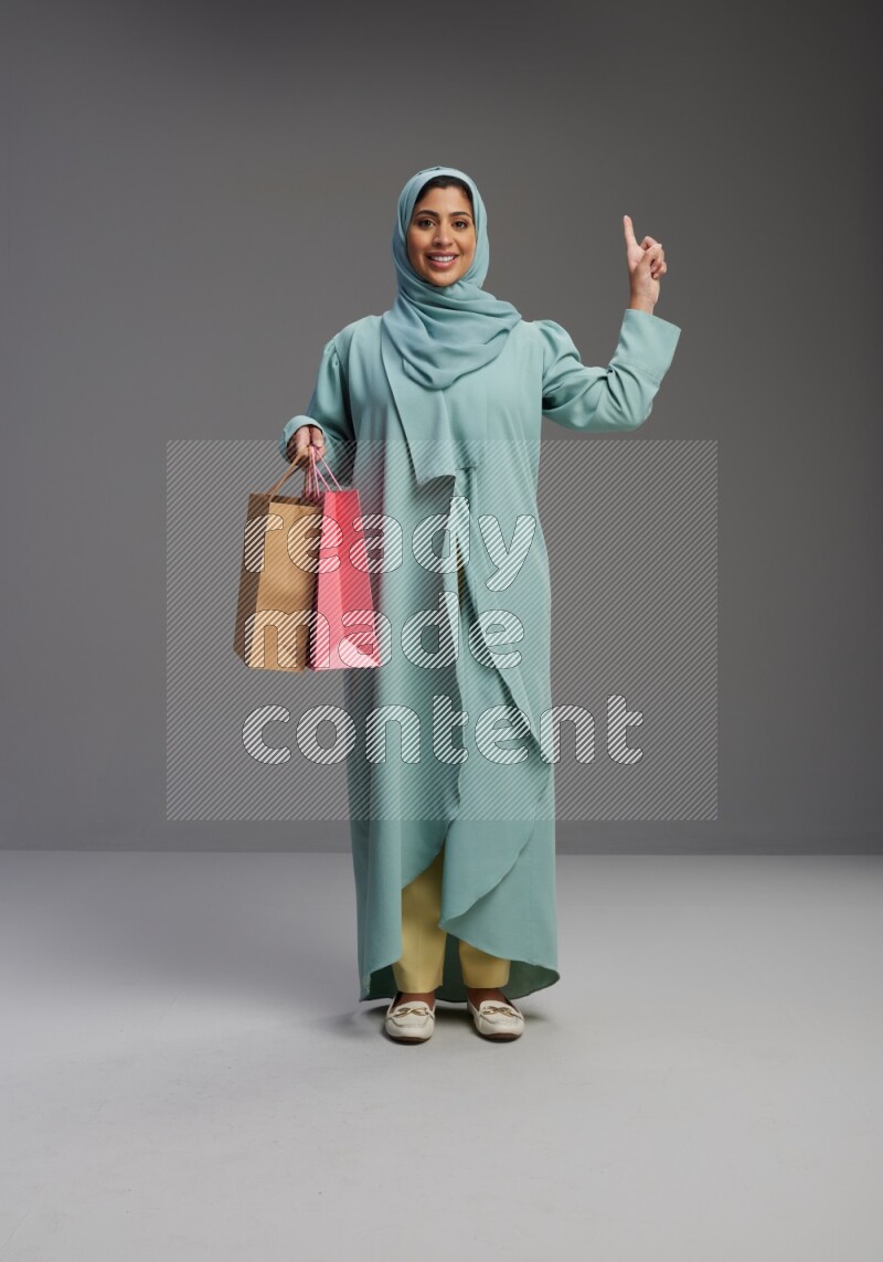 Saudi Woman wearing Abaya standing holding shopping bag on Gray background