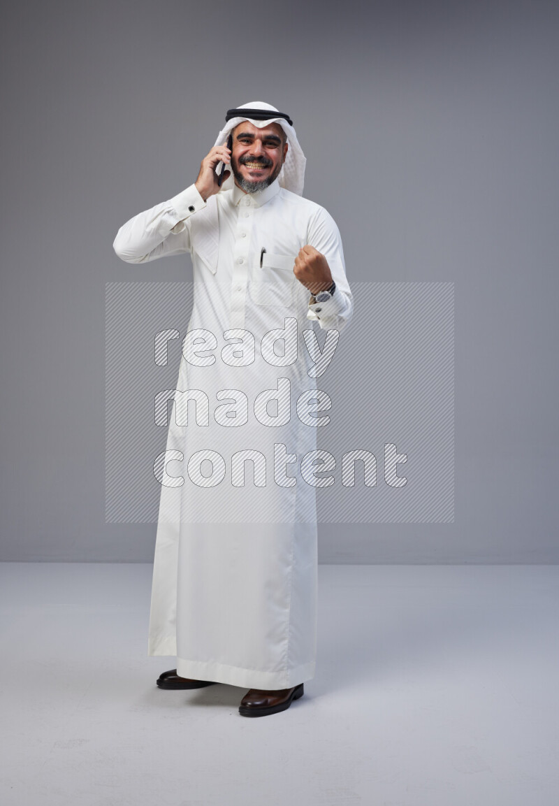Saudi man Wearing Thob and white Shomag standing talking on phone on Gray background
