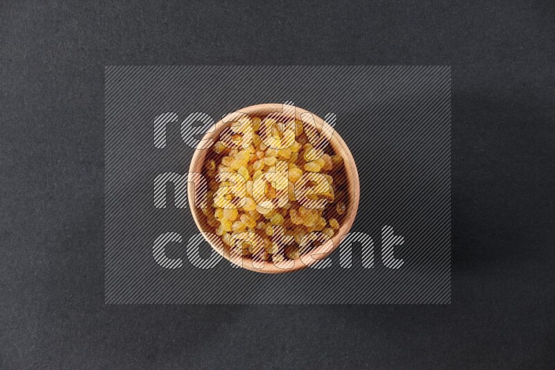 A wooden bowl full of raisins on a black background in different angles
