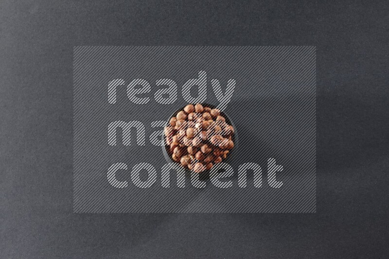 A black pottery bowl full of peeled hazelnuts on a black background in different angles