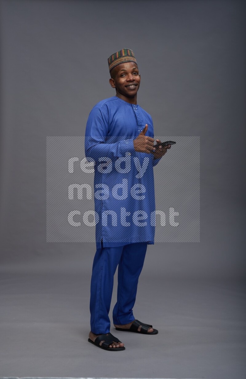 Man wearing Nigerian outfit standing texting on phone on gray background