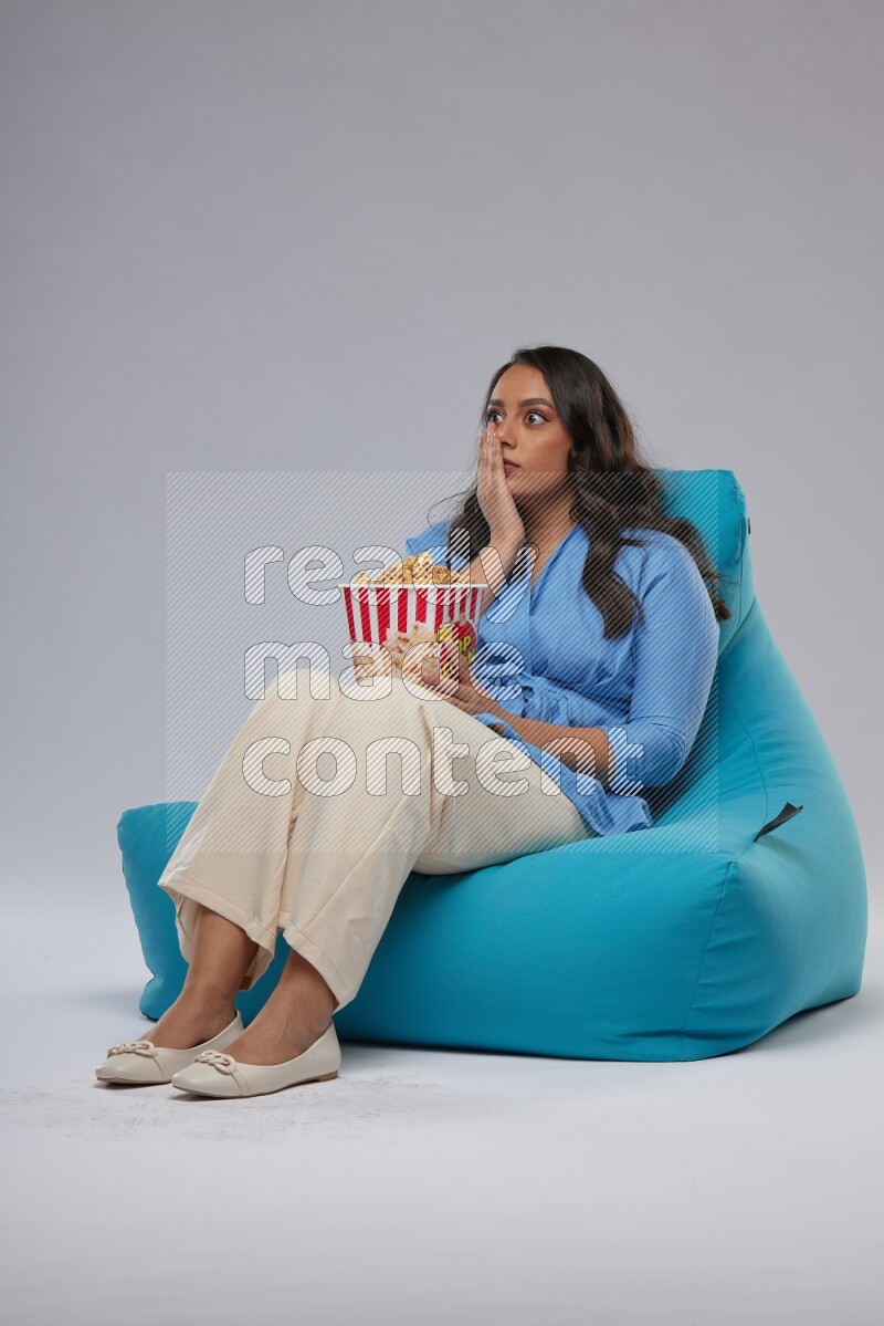 A woman sitting on a blue beanbag and eating popcorn