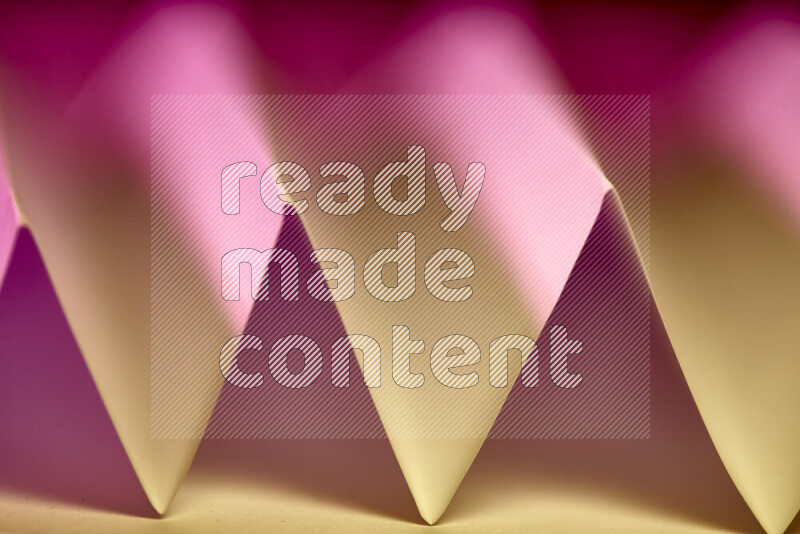 A close-up abstract image showing sharp geometric paper folds in pink gradients and warm tones
