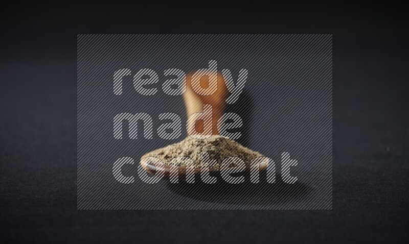 مغرفة خشبية ممتلئة ببودرة الهيل على خلفية سوداء