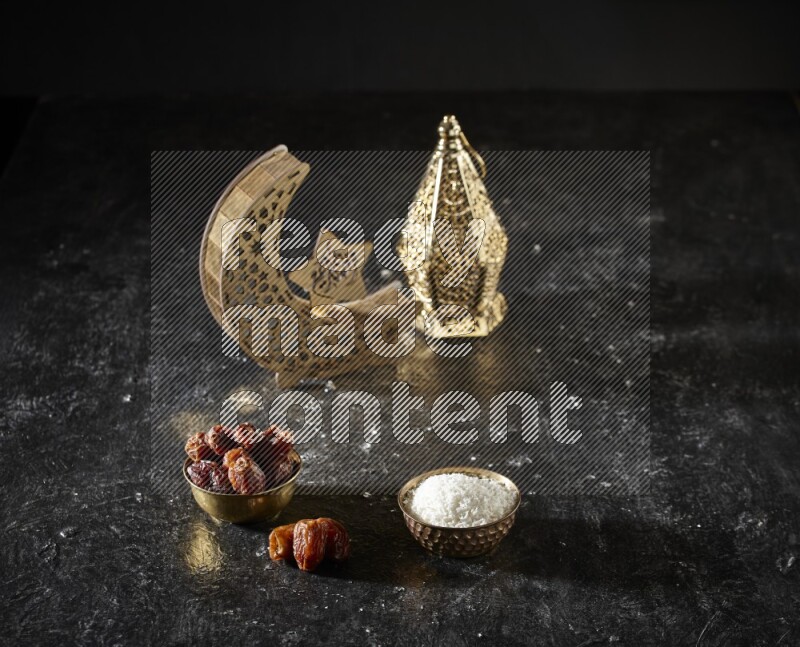 Dates in a metal bowl with desiccated coconuts beside golden lanterns in a dark setup