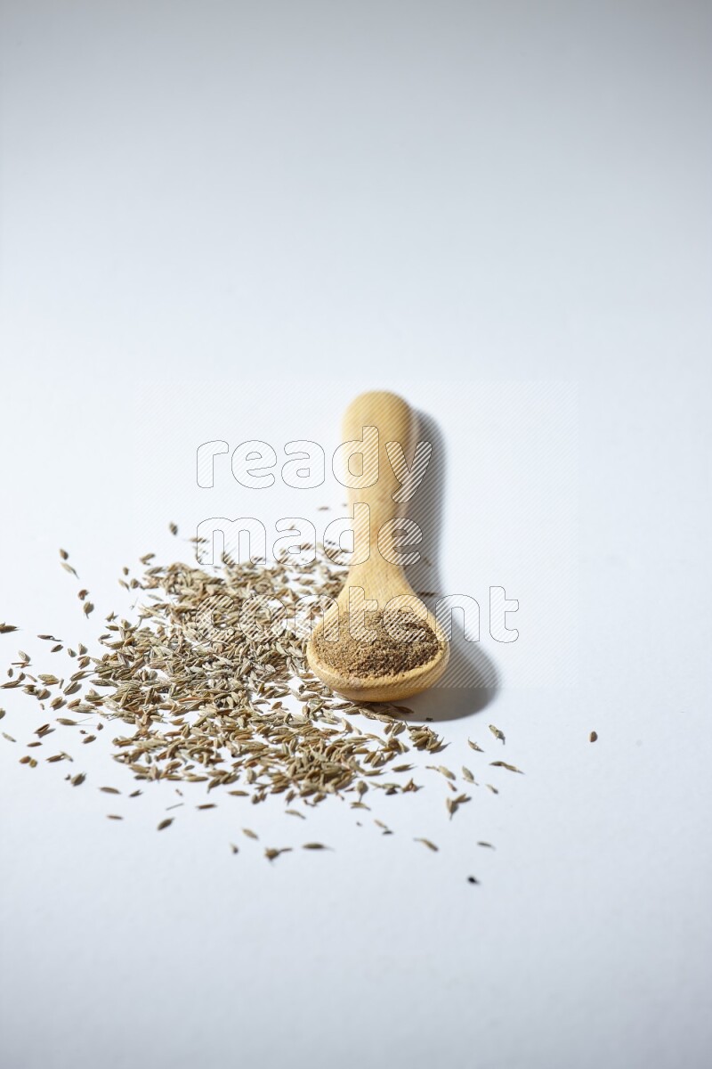 A wooden spoon full of cumin powder and cumin seeds beside it on white flooring