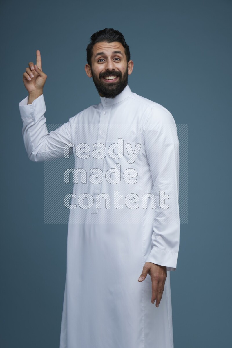 A man pointing in a blue background wearing Saudi Thob