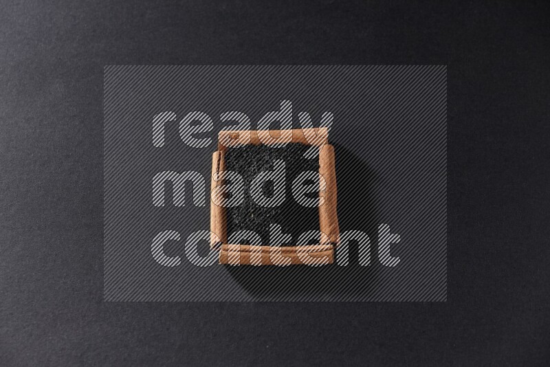 A single square of cinnamon sticks full of black seeds on black flooring