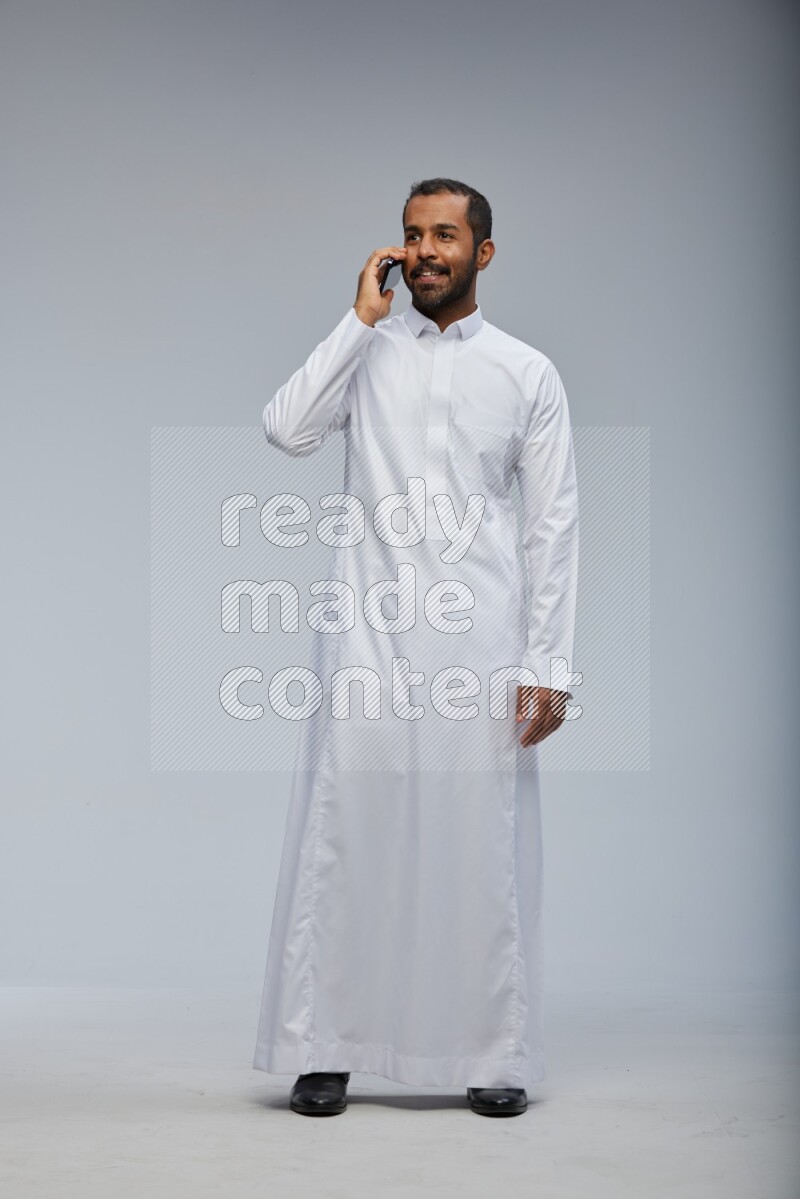 Saudi man wearing Thob standing talking on phone on Gray background