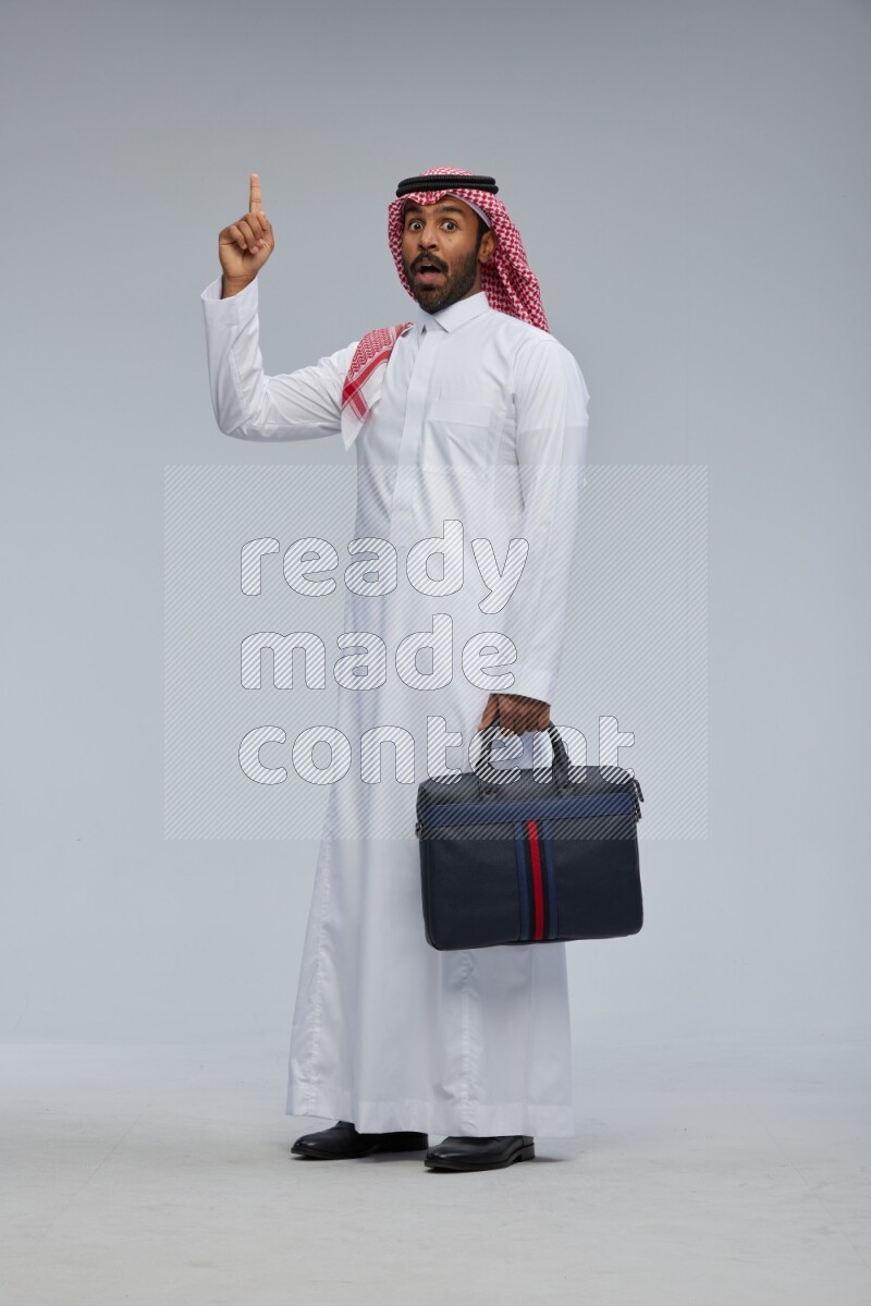 Saudi man Wearing Thob and shomag standing holding bag on Gray background