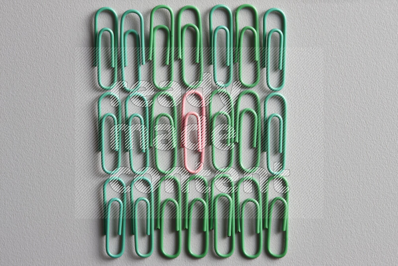 A bunch of green paper clips with a different colored paper clip in the center on grey background