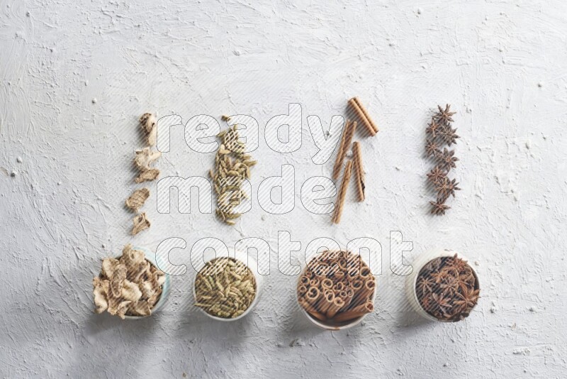 Cardamom, ginger, cinnamon sticks and star anise in 4 bowls on a textured white background
