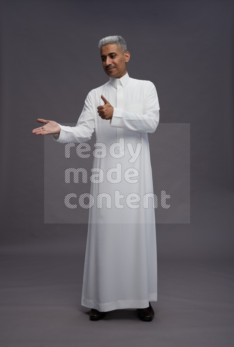 Saudi man wearing thob standing interacting with the camera on gray background