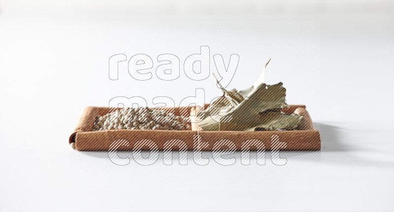 مربعان من أعواد القرفة ممتلئان بحبوب الفلفل الأبيض وأوراق الغار علي خلفية بيضاء