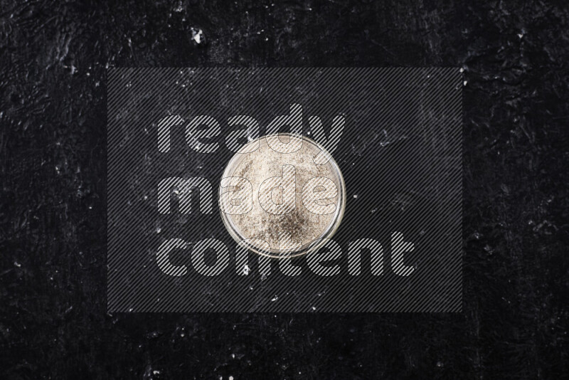 A glass jar full of onion powder on black background