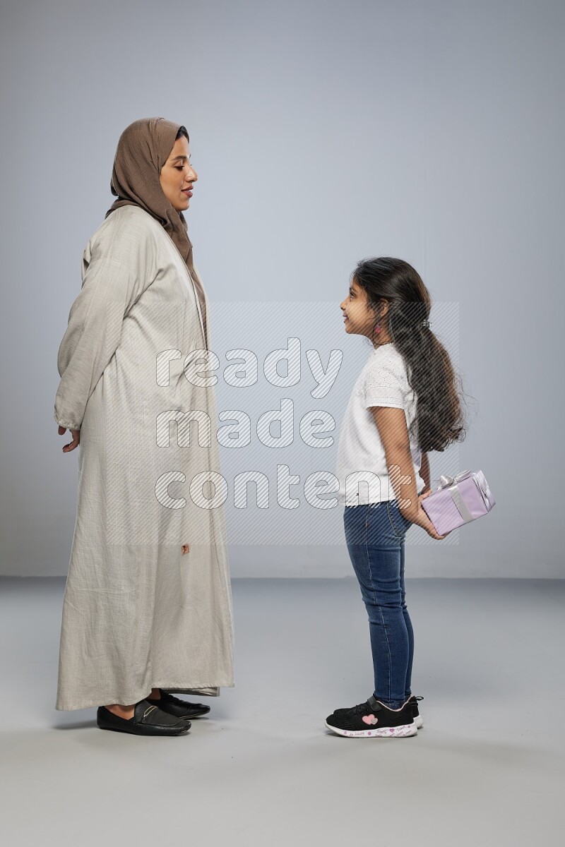 A girl standing hiding a gift behind her back for her mother on gray background