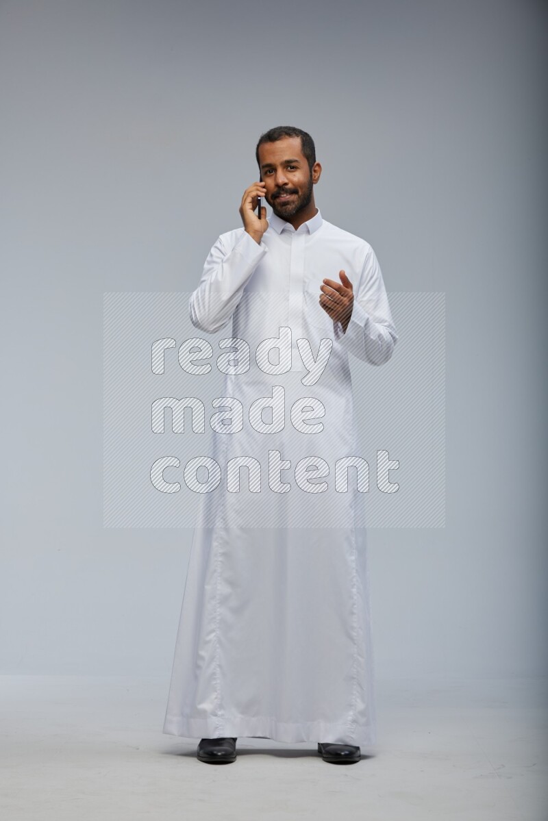 Saudi man wearing Thob standing talking on phone on Gray background