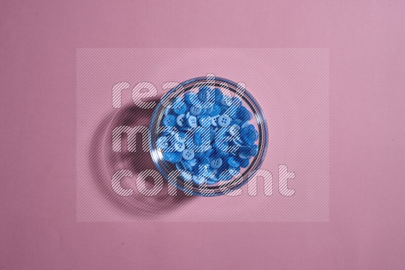 Colored buttons in a glass bowl on rose background