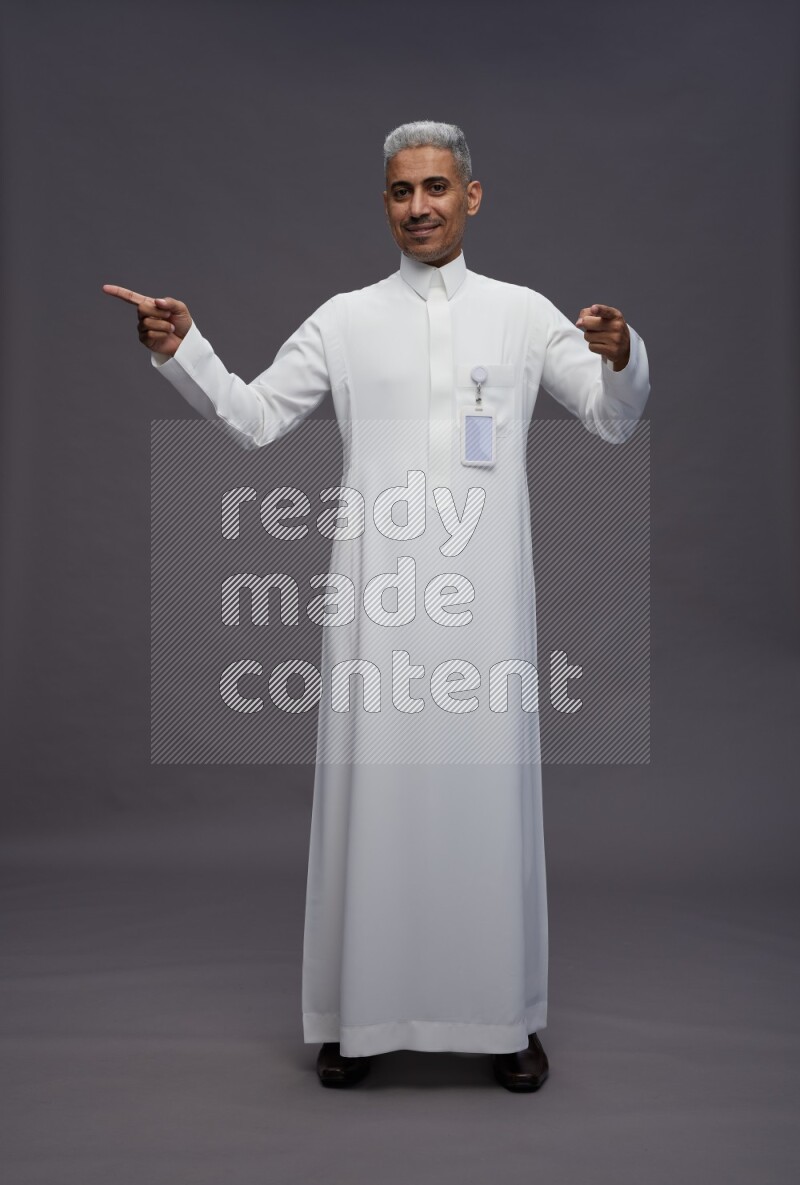 Saudi man wearing thob with pocket employee badge standing interacting with the camera on gray background