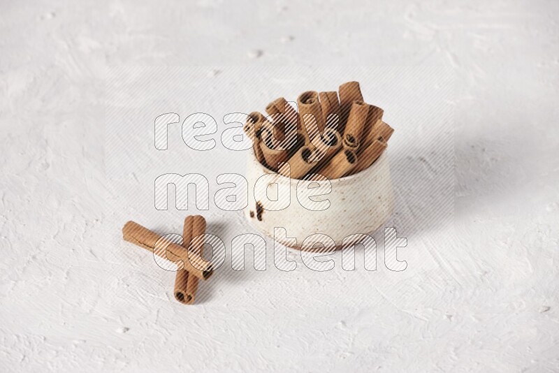 Cinnamon sticks in a beige bowl on a white background
