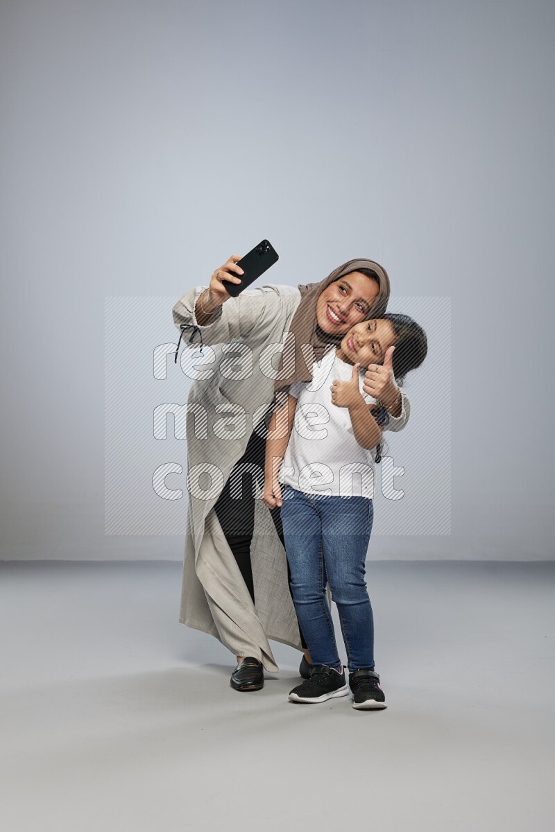 A girl standing taking selfie with her mother on gray background