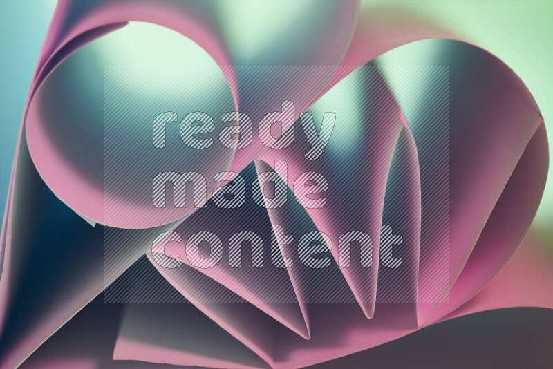An artistic display of paper folds creating a harmonious blend of geometric shapes, highlighted by soft lighting in green and pink tones