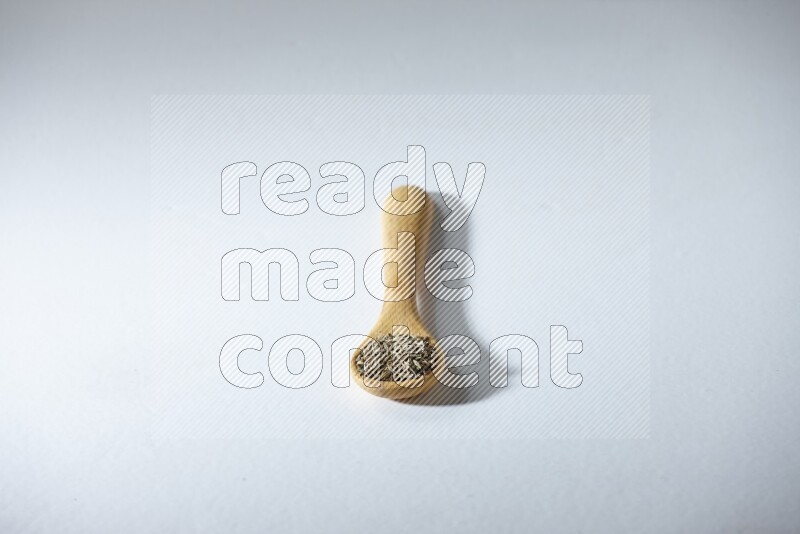 ملعقة خشبية مليئة بحبوب الكمون على خلفية بيضاء