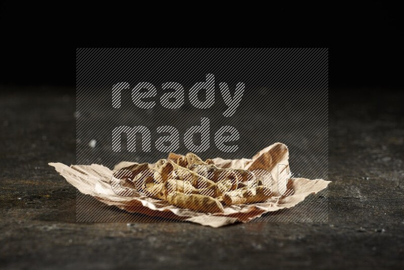 Dried turmeric whole fingers in a crumpled piece of paper on textured black flooring