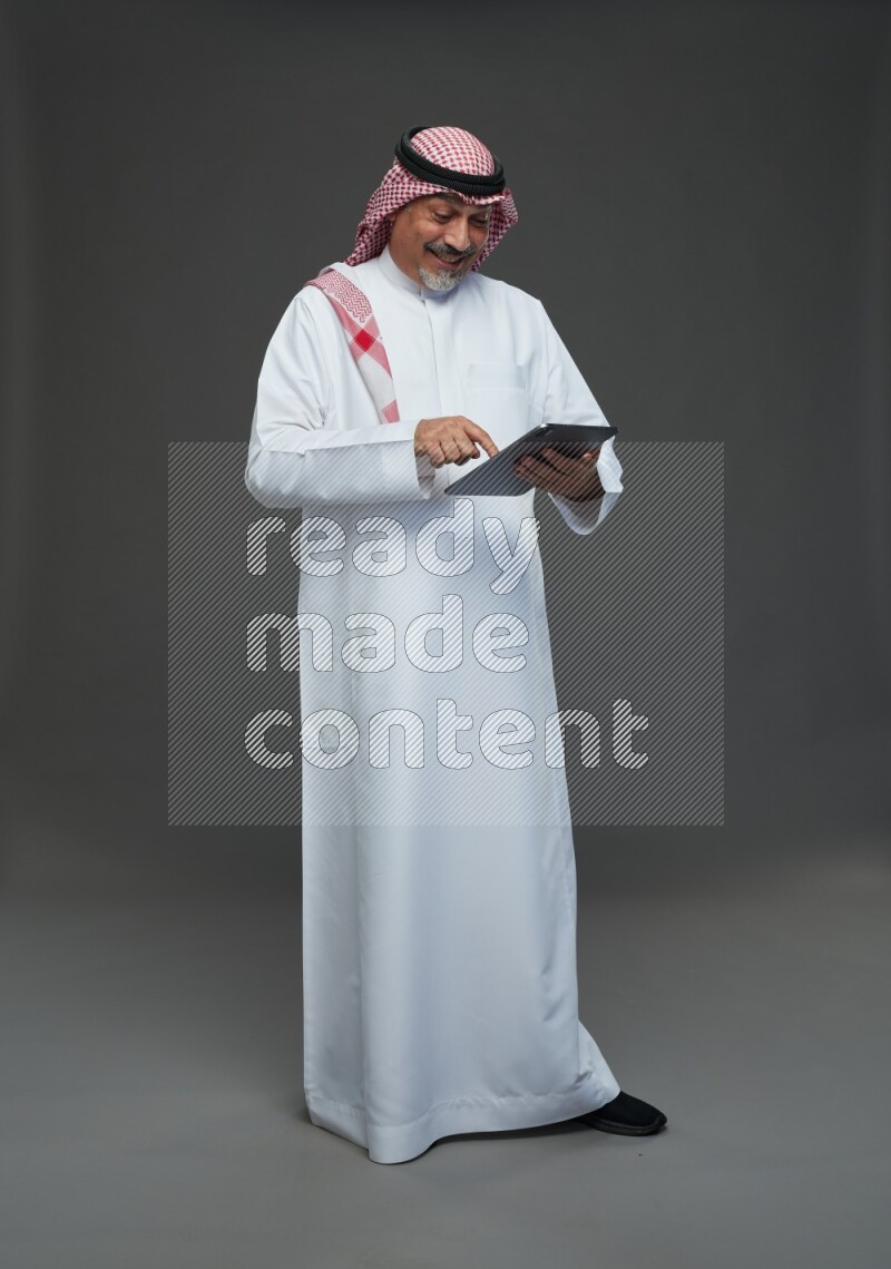 Saudi man with shomag Standing working on tablet on gray background