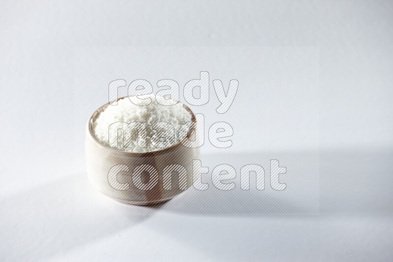 A beige ceramic bowl full of desiccated coconut on a white background in different angles