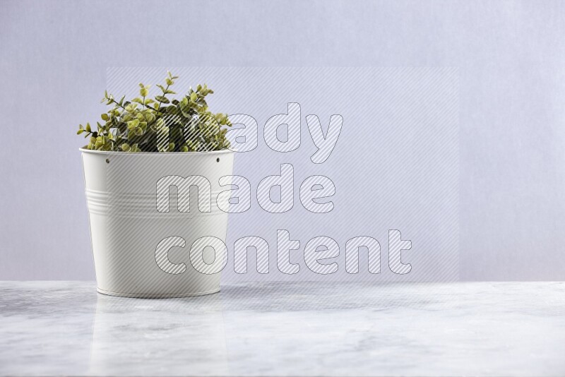 Green artificial plant in white pot on grey marble background