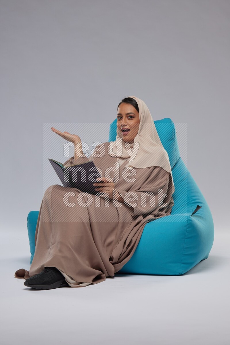 A woman sitting on a blue beanbag and reading a book