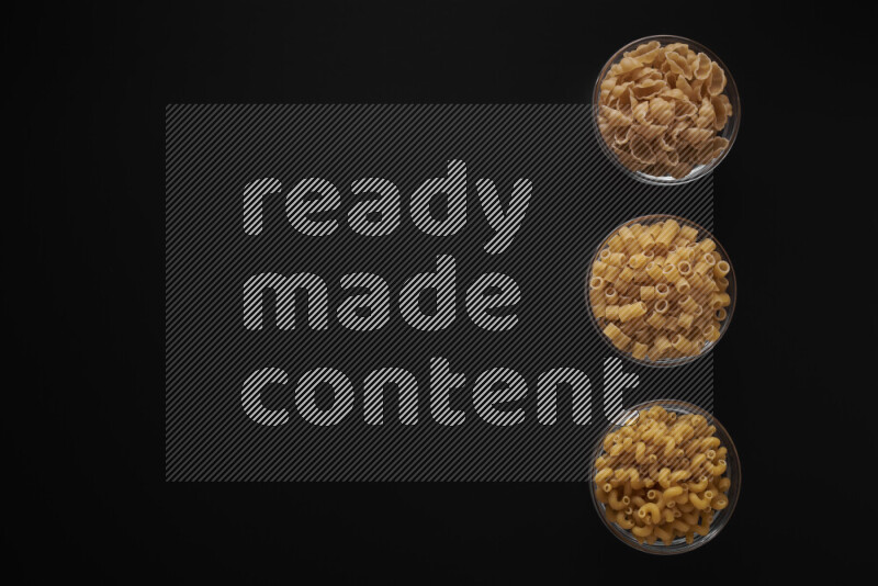 Different pasta types in 3 glass bowls on black background