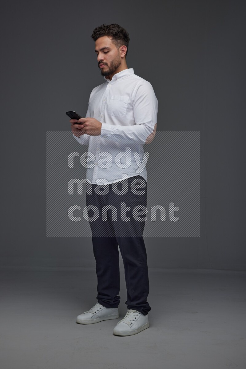 A man wearing smart casual standing and using his phone eye level on a gray background