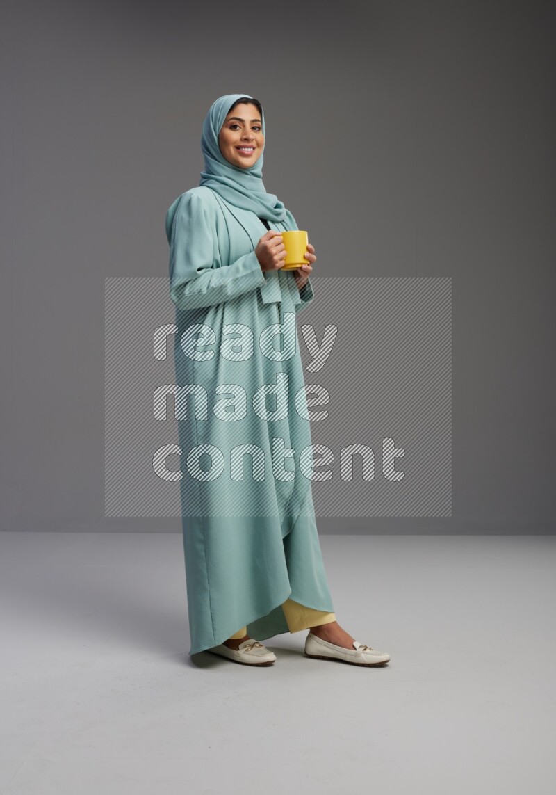 Saudi Woman wearing Abaya standing  holding a mug on Gray background