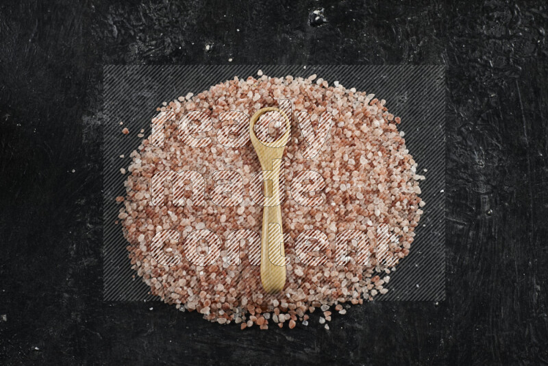 A wooden spoon full of coarse himalayan salt crystals on a bunch of the crystals on black background