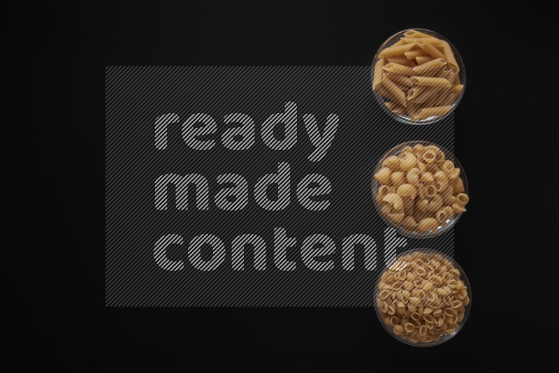 Different pasta types in 3 glass bowls on black background