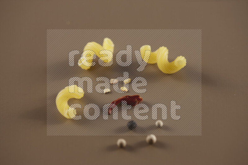Raw pasta with different ingredients such as cherry tomatoes, garlic, onions, red chilis, black pepper, white pepper, bay laurel leaves, rosemary and cardamom on beige background