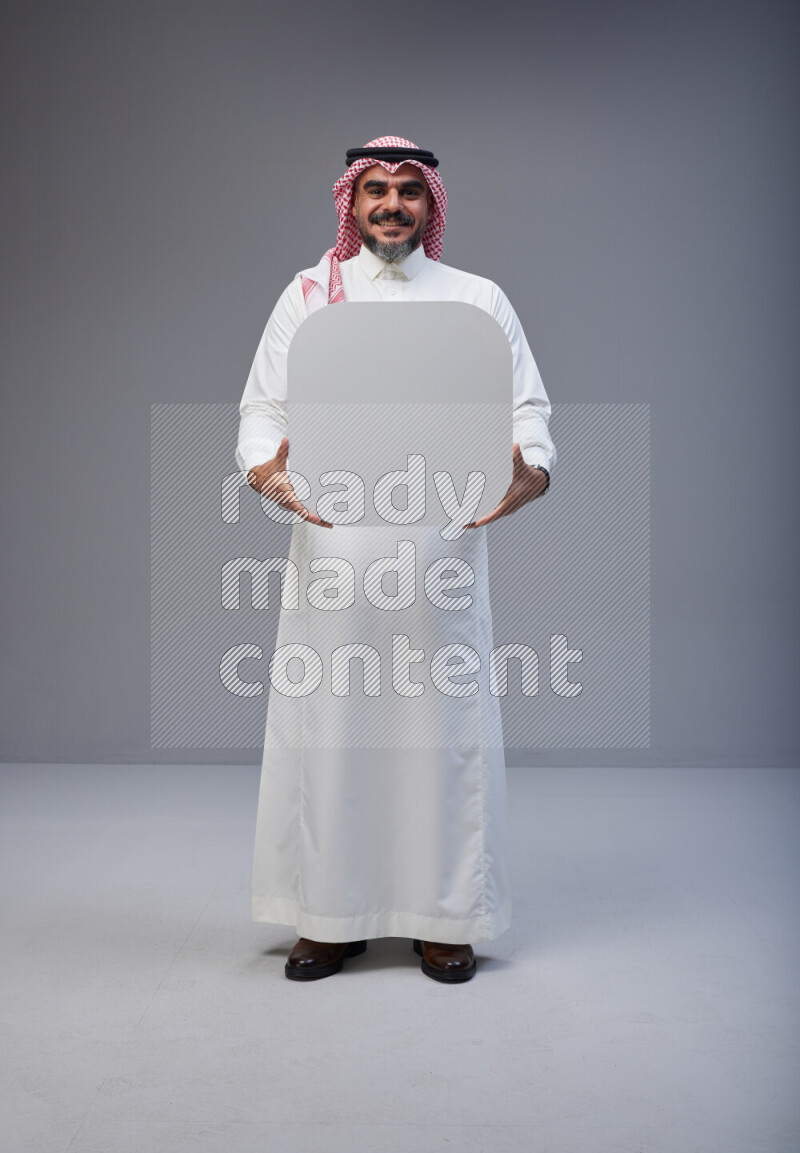 Saudi man Wearing Thob and red Shomag standing holding social media sign on Gray background