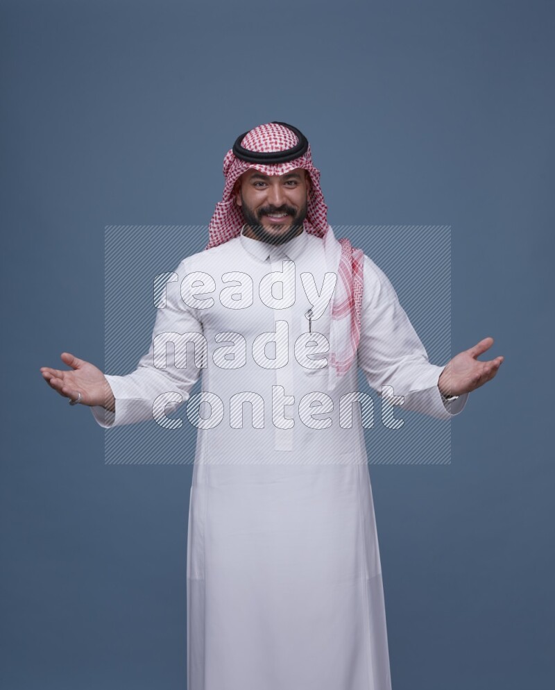 A man pointing on blue background wearing Saudi Thob with Shomag