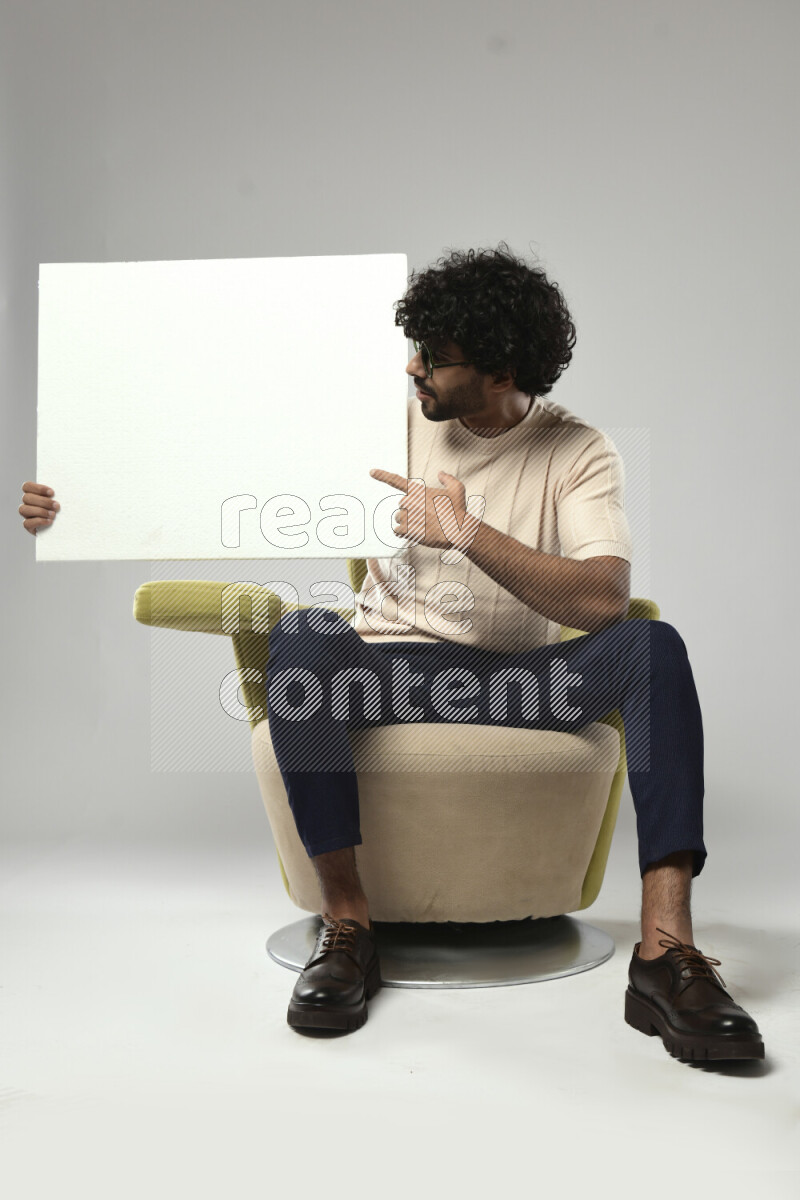 A man wearing casual sitting on a chair holding a white board on white background