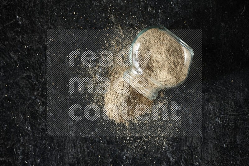 وعاء زجاجي للتوابل مقلوب ممتلئ ببودرة الهيل على خلفية سوداء