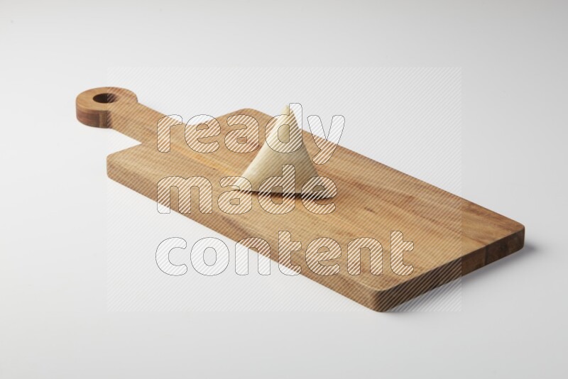 One uncooked samosa on a wooden cutter on a white background