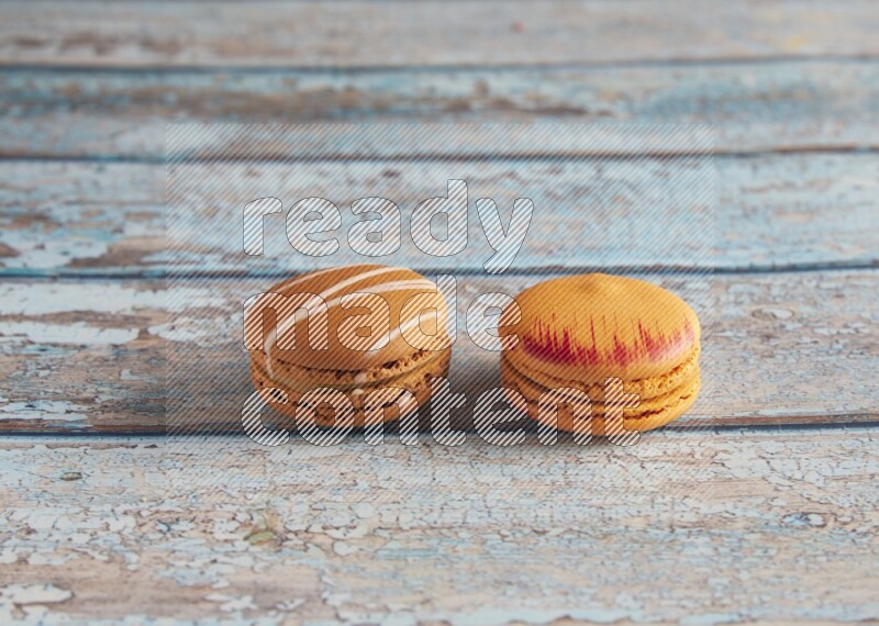 45º Shot of of two assorted Brown Irish Cream, and Orange Exotic macarons on light blue background