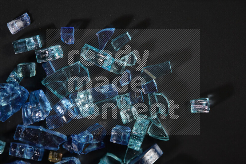 Transparent blue fragments of glass scattered on a black background