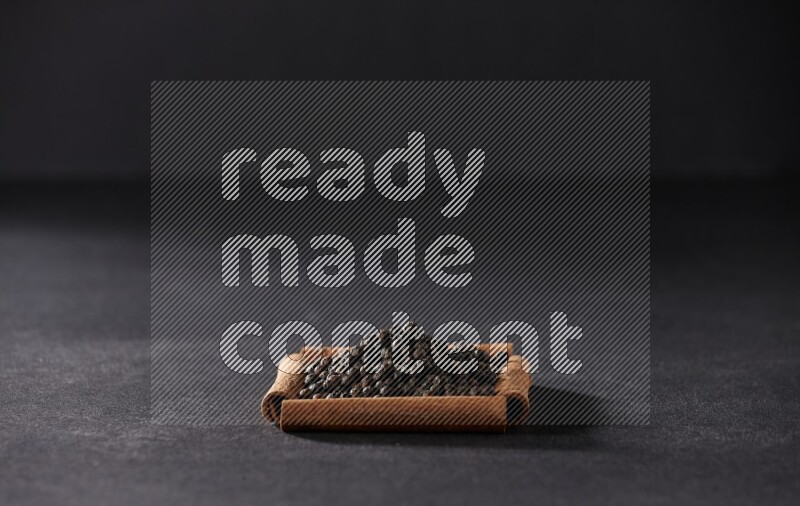 A single square of cinnamon sticks full of black pepper on black flooring