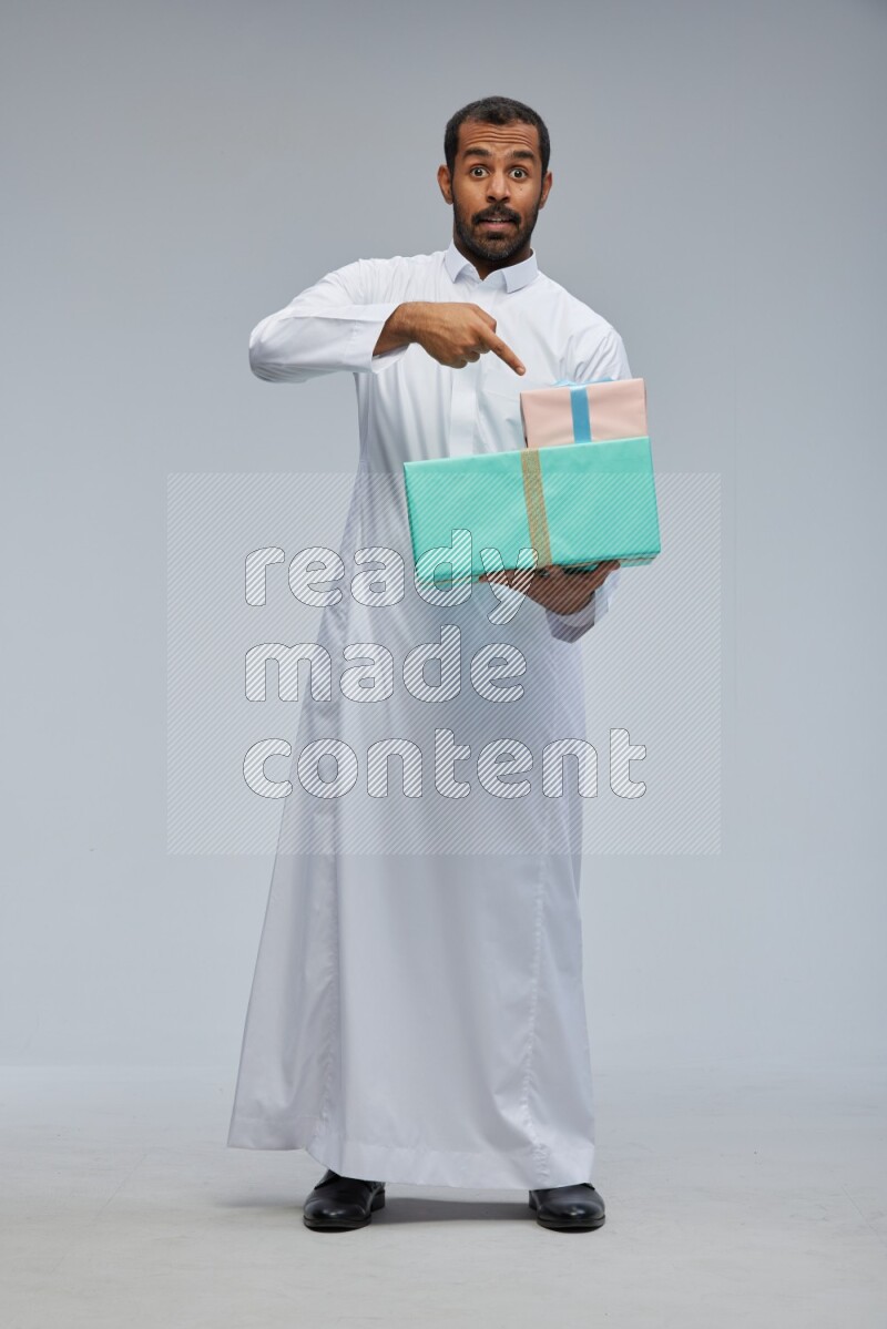Saudi man Wearing thob standing holding gift box on Gray background