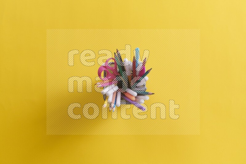 Pens, pencils and school supplies in a metal pen holder on yellow background