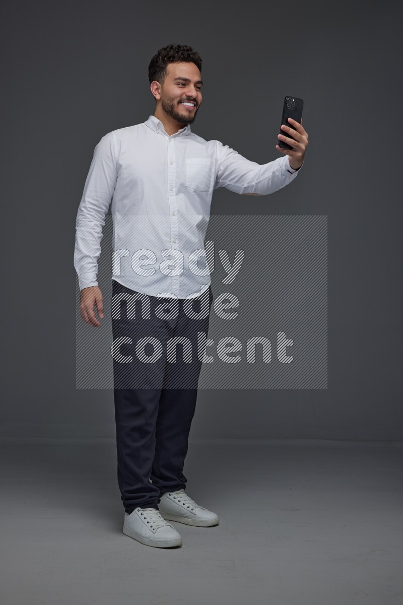 A man wearing smart casual and taking selfie with his phone eye level on a gray background